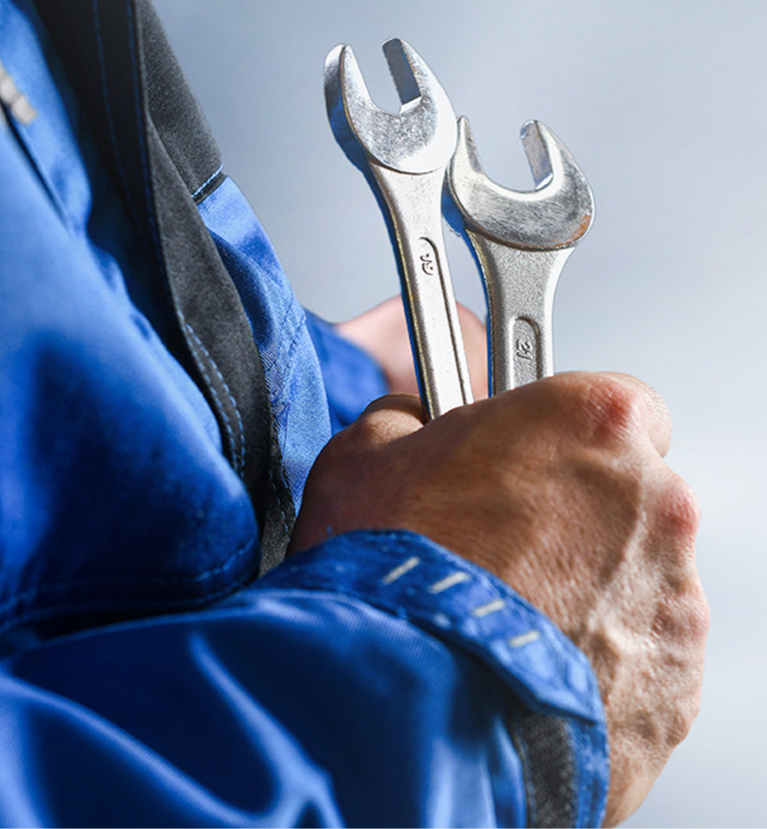 A man in overalls in a garage passing another man a set of car keys.